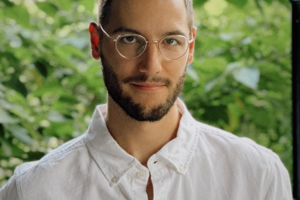 A portrait of a student with glasses on a green background.